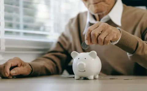 Un anciano deposita una moneda en una hucha, preparándose para la jubilación obligatoria.