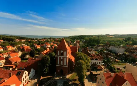 Widok na urokliwe Tolkmicko z charakterystyczną wieżą kościelną. Wśród czerwonych dachów i zieleni rozciąga się malowniczy krajobraz, idealny na odkrywanie tolkmickich atrakcji.