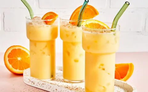 Drei cremige, eisgekühlte Painkiller Cocktails mit Orangenscheiben und grünen Strohhalmen auf einem Terrazzo-Tablett.