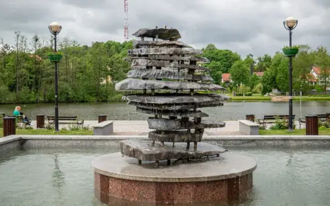 Kamienna rzeźba-fontanna nad jeziorem, jedna z atrakcji Czosu. W tle drzewa i budynki.