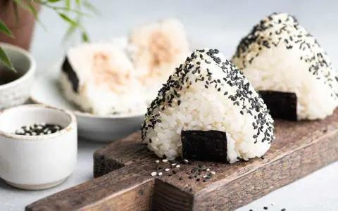 Trójkątne onigiri sushi z czarnym sezamem i kawałkiem nori na drewnianej desce.
