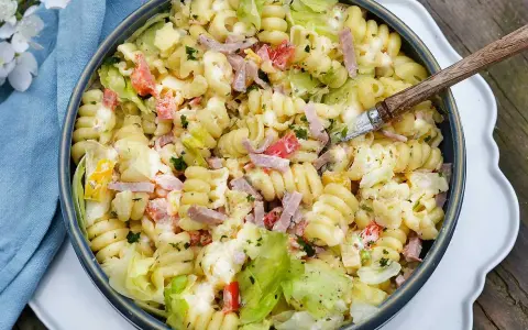 En stor skål med krämig pastasallad med skinka, grönsaker och örter. Perfekt för en sommarlunch!