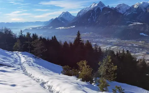 Schneebedeckte Berge über Innsbruck im Winter. Eine Spur führt durch den Schnee bergab, vorbei an dunklen Tannen.
