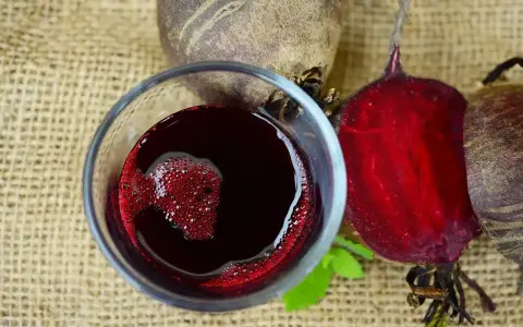 Verre de jus de betterave rouge vif, avec des betteraves entières et coupées autour. Une boisson saine pour savoir comment faire du jus de betterave.