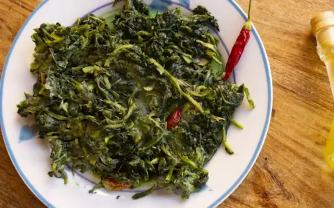 Un piatto di cicoria in padella, condita con peperoncino rosso e un filo d'olio d'oliva, su un tavolo di legno.