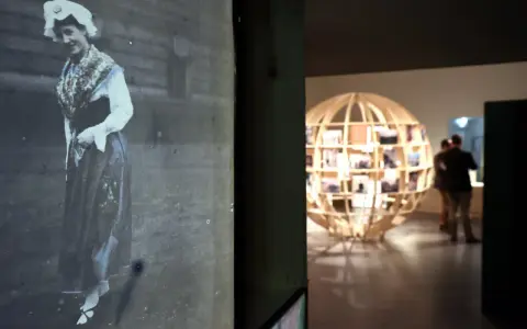 Exposition Albert Kahn : une femme en costume traditionnel sur une photo ancienne, un globe de bois rempli de clichés en arrière-plan.