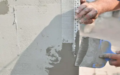 Mani esperte applicano stucco e rete per stuccare angolo muro, garantendo una finitura perfetta.