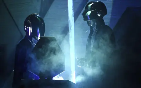 Medlemmar av Daft Punk i sina ikoniska hjälmar, omgivna av rök och blått ljus på scenen.