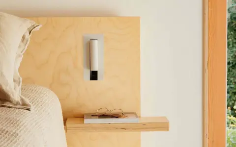 Applique murale au design épuré, à la bonne hauteur pour une tête de lit en bois clair. Lunettes posées sur un livre.