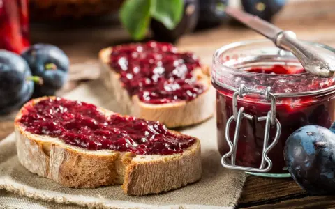 Frisches Brot mit Pflaumenmarmelade ohne Zucker, daneben eine Einmachglas gefüllt mit der leckeren Marmelade und frische Pflaumen.