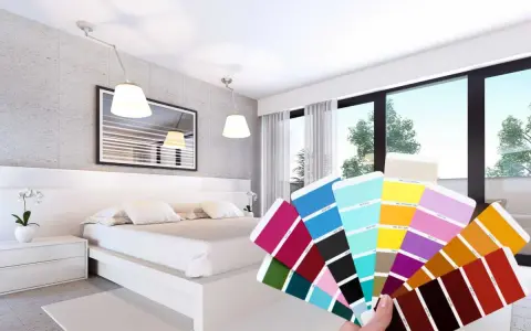 Una mano tiene un campionario di colori davanti a una moderna camera da letto bicolore, con pareti grigie e bianche e un letto bianco.
