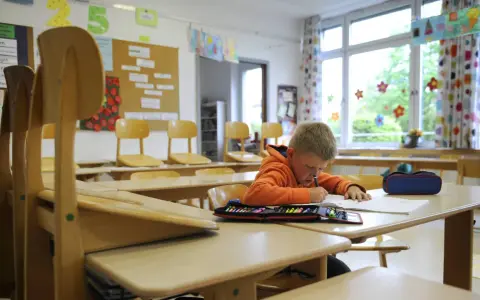Ein Junge lernt allein im Klassenzimmer. Die leeren Stühle erinnern an eine kollektivstrafe, die er nicht verdient hat.