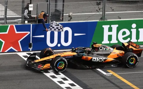 El coche de McLaren cruza la meta en el **Gran Premio Países Bajos**. El piloto celebra la victoria ondeando la bandera a cuadros.