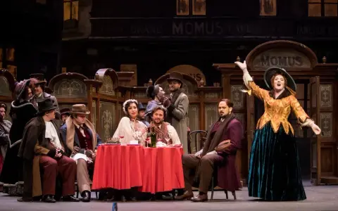 Scena z operetki. Kobieta w żółtej sukni śpiewa na tle kawiarni "Momus".