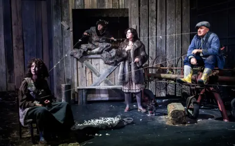 Scena z dramatu. Cztery postacie w wiejskiej scenerii, napięcie w powietrzu. Co to za dramat?