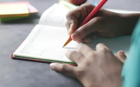 Dłoń pisze w zeszycie, co to dysgrafia? Trudności z pisaniem mogą dotyczyć każdego.