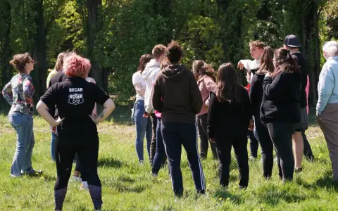 Groupe de jeunes adultes debout dans un champ verdoyant, certains se regardent.