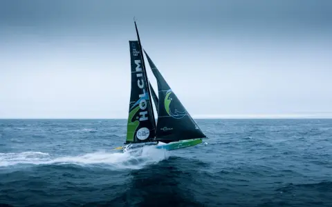 Segelboot des **Team Holcim** pflügt durch die Wellen, die Segel sind mit dem Logo und "The Ocean Race" beschriftet.