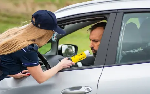 Policjantka mierzy kierowcy alkomatem, sprawdzając, czy nie przekroczył dopuszczalnego limitu promili.