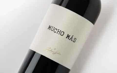 Ciemna butelka wina Mucho Mas, z etykietą z napisem "Mucho Más" i złotym podpisem "Felix Solis".