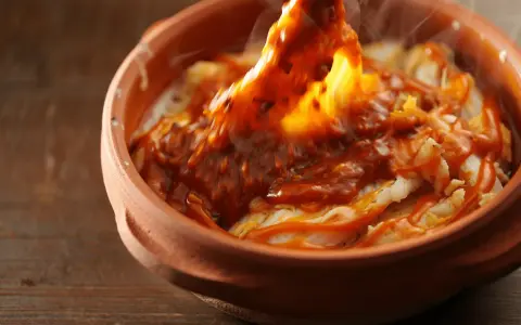 Cocochas de bacalao cubiertas con una salsa roja y burbujeante en una cazuela de barro.
