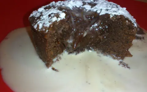 Un fondant au chocolat dégoulinant, saupoudré de sucre glace, servi dans une sauce crémeuse sur une assiette rouge.