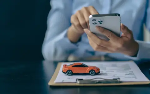 Pomarańczowy mini **casco** na dokumentach, obok dłoni trzymającej smartfon.