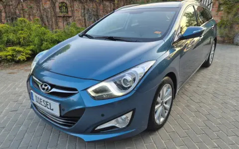 Niebieski Hyundai i40 1.7 CRDi na podjeździe z kostki brukowej, z tyłu ceglany mur porośnięty bluszczem.