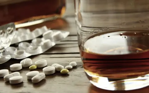 Tabletki i szklanka z alkoholem. Zastanawiasz się, po jakim czasie od zastrzyku można pić alkohol? To ważne pytanie.