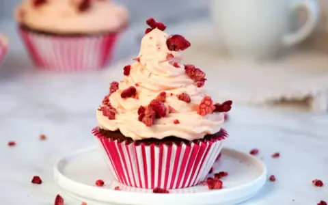Ein köstlicher Red Velvet Muffin mit rosa Frosting und gefriergetrockneten Himbeeren, perfekt für ein Red Velvet Muffins Rezept.