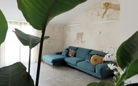 Divano turchese in un salotto con carta da parati a tema giungla e piante rigogliose, per un perfetto **stile jungle chic**.