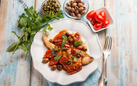 Un saporito pesce spada alla siciliana, condito con pomodorini, olive e capperi, guarnito con menta fresca.
