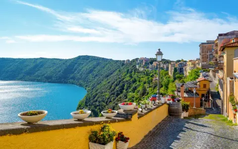 Widok na jezioro i zielone wzgórza z kolorowymi domami w Castel Gandolfo.
