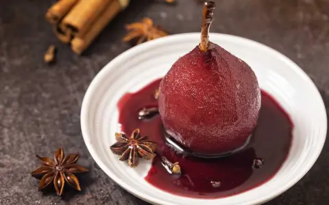 Peras al vino tinto, cocidas con especias como anís estrellado y canela, servidas en un plato blanco con su sirope.