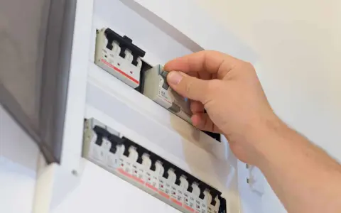 Main disjoncteur général manipulé par une main dans un tableau électrique blanc.
