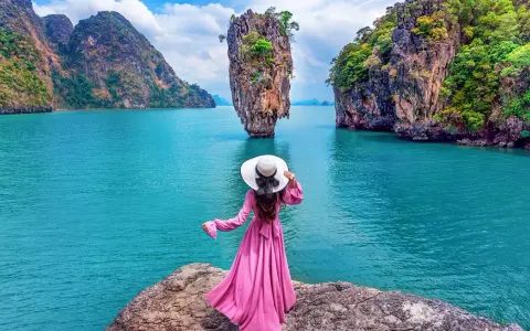 Donna con abito rosa e cappello bianco ammira la spettacolare **isola di James Bond** con le sue formazioni rocciose uniche e il mare turchese.