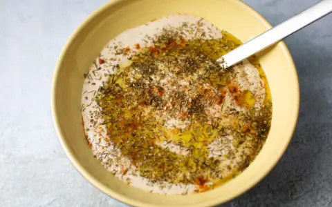 Cremiger Hummus Aufstrich in gelber Schüssel, beträufelt mit Olivenöl und bestreut mit Kräutern und Paprika.