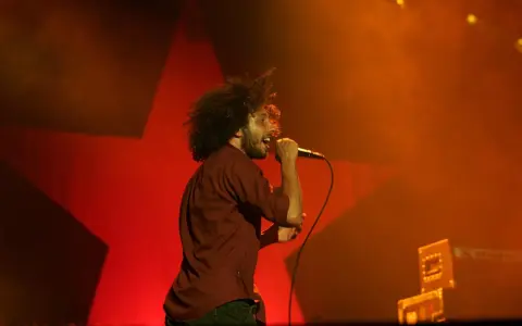 Zac Zack de la Rocha śpiewa z pasją na koncercie Rage Against the Machine. Czerwona gwiazda w tle podkreśla energię występu.