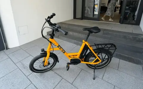 Gelbes i:SY E-Bike, das bei der Stiftung Warentest gut abgeschnitten hat, steht auf gepflastertem Untergrund vor einer Treppe.