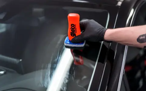 Rękawiczka z czarną rękawiczką nakłada preparat na szybę. To pokazuje, jak działa powłoka hydrofobowa, co to znaczy, że woda spływa.