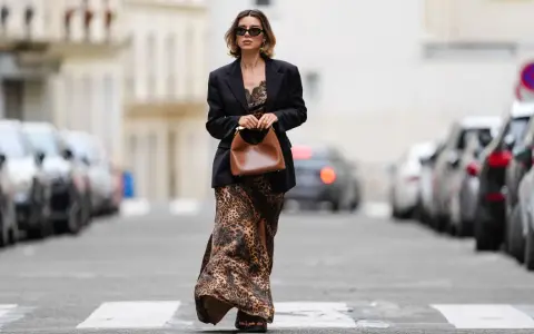 Mujer con un elegante outfit de domingo primavera: vestido largo de leopardo, blazer negro y bolso marrón.
