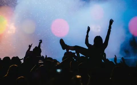 Tłum na jednym z największych festiwali muzycznych na świecie. Kobieta na rękach, ręce w górze, światła sceny.