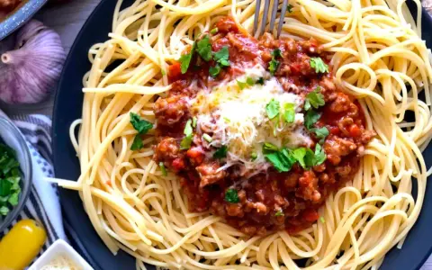Spaghetti bolognese, prosty przepis. Aromatyczny sos mięsny z mielonym mięsem i pomidorami na złocistym makaronie, posypany serem i natką pietruszki.