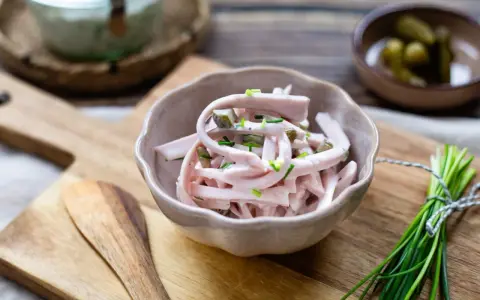 Schmackhaftes Fleischsalat Rezept mit Gurkenstückchen und Schnittlauch garniert, serviert in einer Schale auf einem Holzbrett.