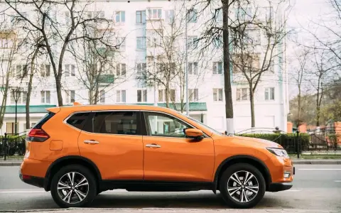 Pomarańczowy SUV do 50 tys. zaparkowany na tle białego budynku i drzew.