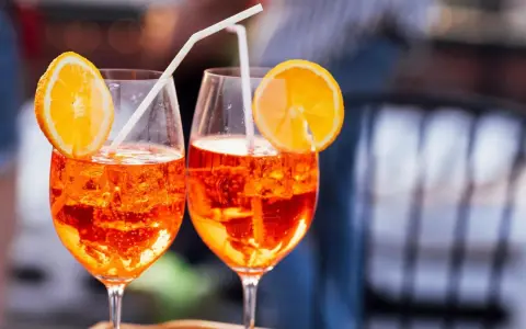 Zwei Aperol Spritz mit Orangenscheiben und Strohhalmen. Der leuchtende Aperol Farbstoff schimmert in den Gläsern.