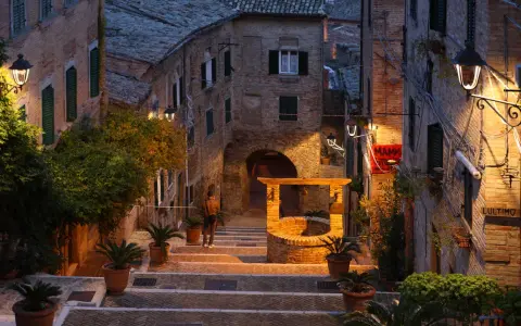 Antica scala a Gabicce Monte illuminata da lampioni, con un pozzo in mattoni e piante in vaso.