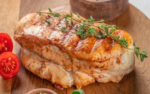 Soczysty filet z indyka, pieczony z ziołami, podany z pomidorkami koktajlowymi na drewnianej desce.