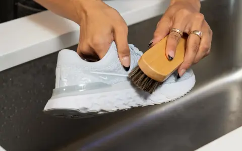 Mani che puliscono una scarpa da ginnastica bianca con una spazzola, mostrando come lavare le tn bianche per farle tornare come nuove.