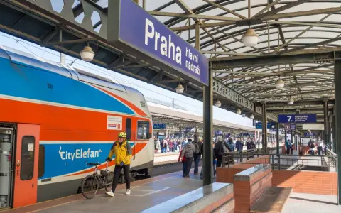Pociąg z Gdańska do Pragi na dworcu głównym. Mężczyzna w żółtej kurtce z rowerem czeka na peronie.